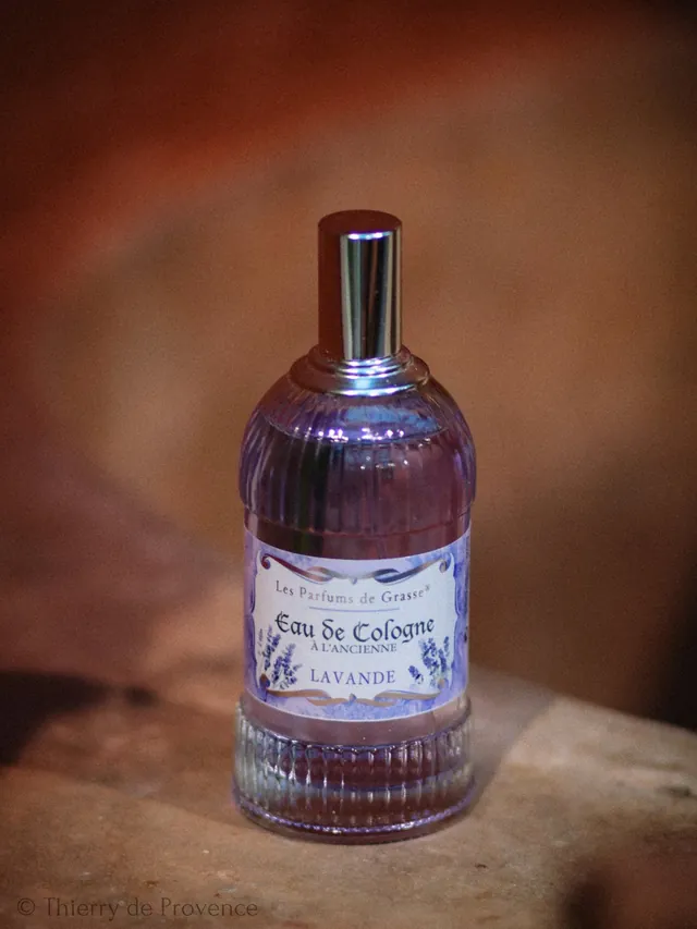 Laventeli-Eau de Cologne-pullo puiset taustat. Pullossa violetti etiketti, teksti "Eau de Cologne". Tunnelma on elegantti.