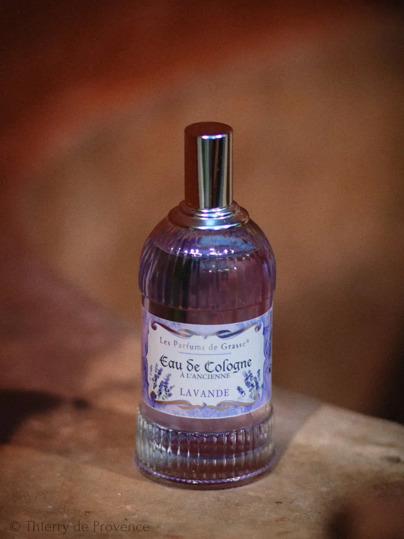 Laventeli-Eau de Cologne-pullo puiset taustat. Pullossa violetti etiketti, teksti "Eau de Cologne". Tunnelma on elegantti.